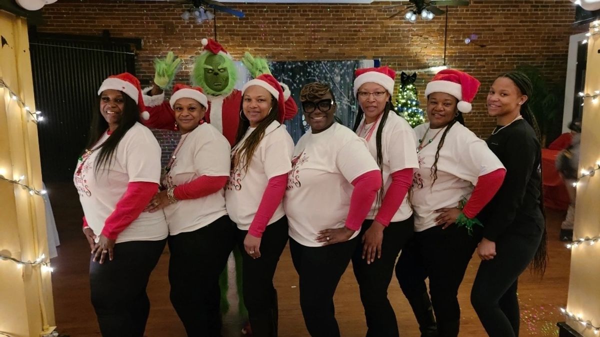 Volunteers in Santa hats posing with the Grinch at the Santa's Wonderland community event